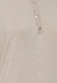 Beige striktop med en lukning med tre metalliske knapper. Glat tekstur med en diskret glans. Simpelt og alsidigt design.