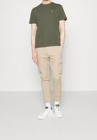 Olivengrøn kortærmet t-shirt, khakifarvede cargobukser med sidelommer og hvide sneakers med grønne detaljer. Enkel, afslappet påklædning.