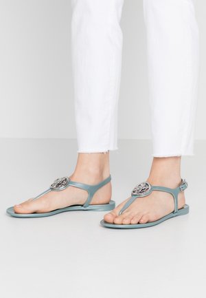 Płaskie sandały z miękkiego niebieskiego materiału, z paskiem w kształcie litery T i okrągłym metalowym zdobieniem na cholewce.