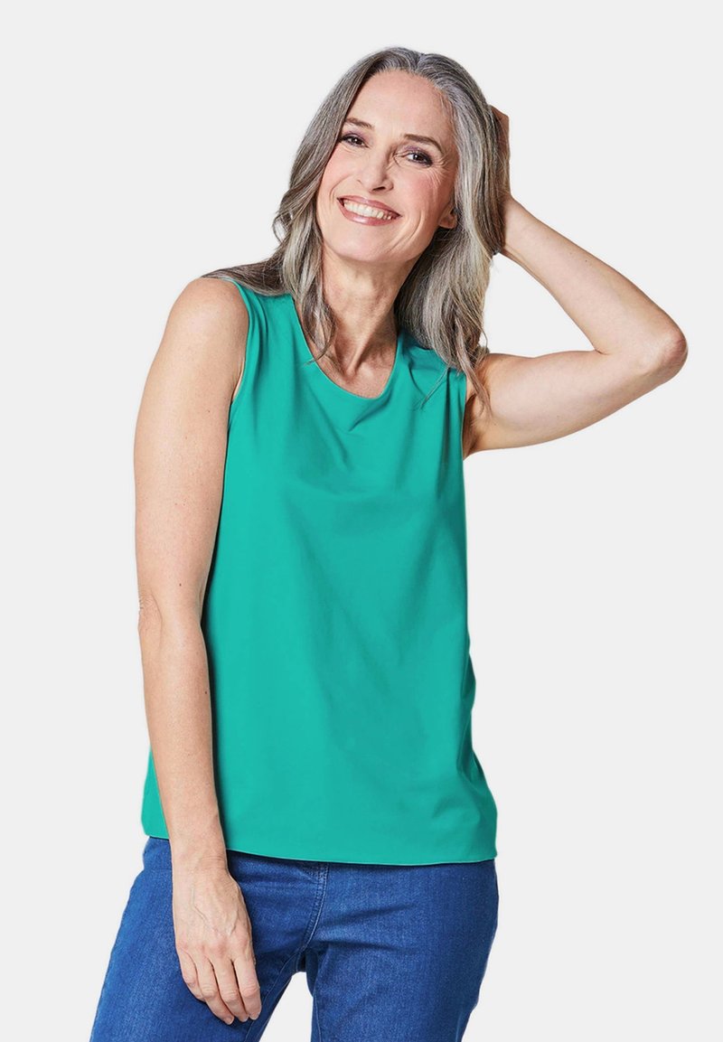 Mouwloze teal blouse met een ronde halslijn en een zachte textuur, gecombineerd met blauwe jeans. De stof lijkt licht en soepel.