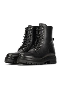 Botas de tobillo de cuero negro con punta redonda, detalles de cordones en la parte frontal, ojales de metal y suela gruesa de goma. Textura suave con acentos de costura.