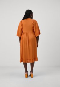 Vestido laranja até ao joelho com acabamento texturizado, mangas largas e bainha com volantes. Combinado com sandálias de salto coloridas.