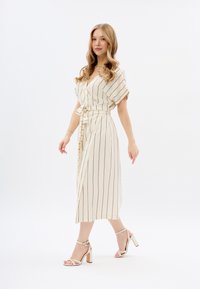 Beige Midikleid mit schwarzen vertikalen Streifen, Wickeldesign, Taillengürtel und kurzen Ärmeln. Getragen mit Sandalen mit Blockabsatz.