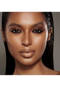 Närbild av ett ansikte med slät, strålande hy. Funktioner inkluderar välformade ögonbryn, mörk eyeliner och glansiga nakna läppar. Håret är slätt och rakt.