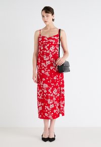 Abito midi rosso floreale con spalline sottili, caratterizzato da un corpino aderente e gonna svasata. Abbinato a una piccola borsa a tracolla nera e tacchi.