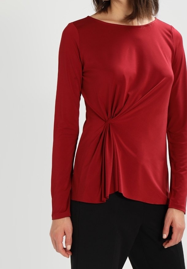 Rotes Langarmoberteil aus weichem Stoff mit einem gedrehten Frontdesign, Rundhalsausschnitt und fließender Form. Kombiniert mit schwarzen Unterteilen.