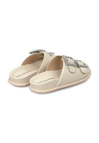 Sandali beige senza strap con una texture morbida e imbottita e dettagli di gioielli sulle cinghie. Presentano una suola testurizzata e un design minimalista.