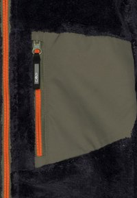 Giacca in pile con tessuto nero soffice e pannelli verde oliva. Presenta dettagli arancioni sulla cerniera e una tasca con cerniera dotata di etichetta con logo.