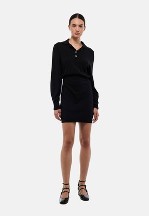 Robe noire en tricot avec un col et trois boutons, design ajusté, manches longues et longueur mini, associée à des chaussures à talons noires.