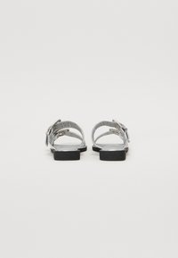 Sandales en cuir gris avec une semelle noire plate, dotées de plusieurs lanières et de boucles en argent pour un ajustement réglable, design minimaliste.