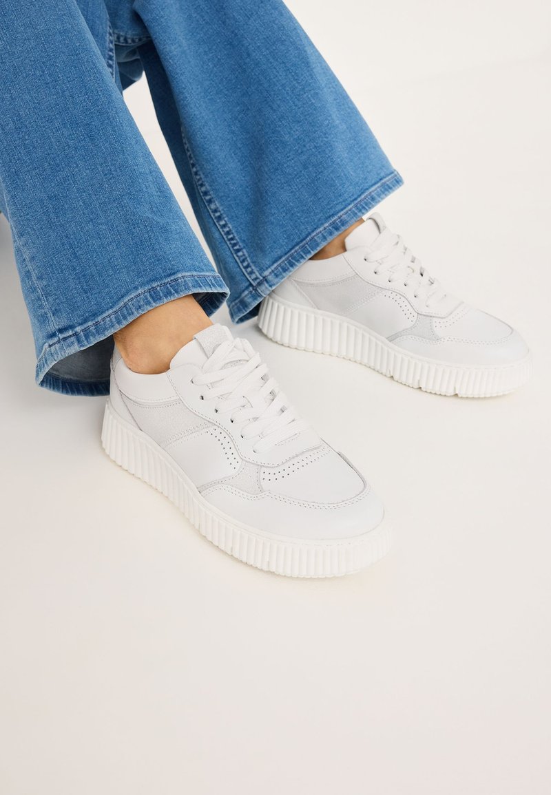 Baskets blanches en cuir texturé avec des accents lisses, comportant une semelle épaisse et striée et un design à lacets, associées à un jean bleu large.