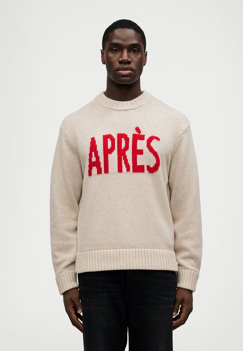 Bežinis megztinis su ryškiu raudonu "APRÈS" tekstu per krūtinę. Riebios rankogaliai ir apvadas suteikia struktūrizuotą detalę.