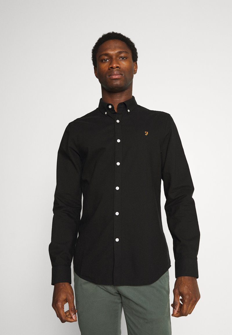 Black button-up shirt with white buttons and a small gold logo on the chest. Features a classic collar and long sleeves, made from smooth fabric.