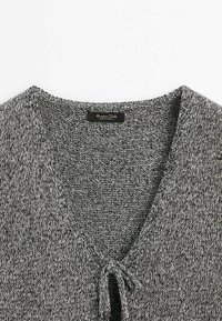 Pull tricoté gris et noir avec col en V et fermeture par nouage à l'avant, affichant une étiquette en tissu au niveau de l'encolure.