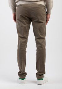 Pantaloni di cotone beige con vestibilità slim, dotati di due tasche posteriori e dettagli di cucitura discreti. Abbinati a sneakers bianche e accenti verdi.