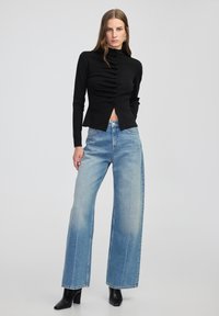 Czarny prążkowany sweter z wysokim kołnierzem i detalem w postaci guzików, zestawiony z luźnymi, jasnoniebieskimi dżinsami o szerokich nogawkach. Uzupełniony czarnymi botkami na obcasie.