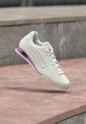 Valge sportlik king, millel on tekstureeritud pealiskate, roosad detailid ja tallas nähtav lilla pehmendusüksus. Paelad on valged; logo on hall.