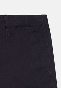 Pantalons en denim foncé avec une texture lisse, un devant plat et une coupe classique. Comprend des coutures détaillées et une taille avec passants de ceinture.