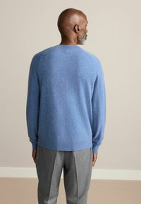 Jasnoniebieski sweter o miękkiej strukturze, z okrągłym dekoltem i ściągaczami, w połączeniu z szarymi, eleganckimi spodniami. Prosty design, brak widocznych wzorów.