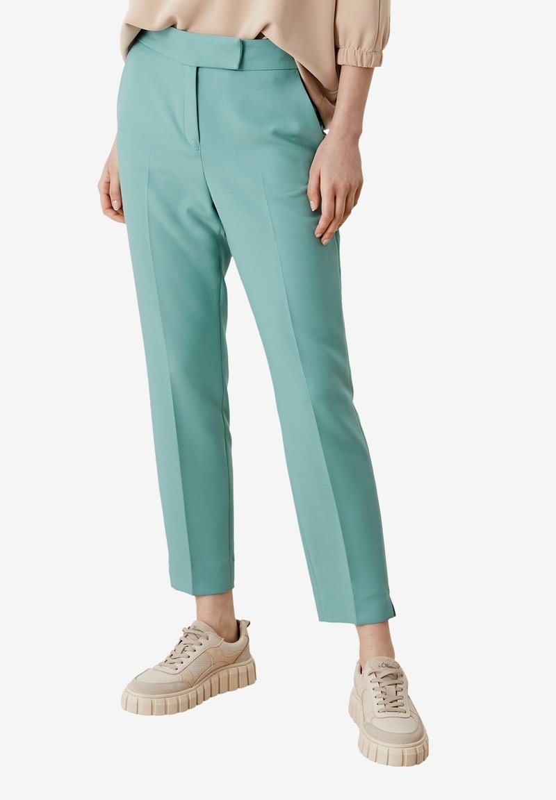 Pantalons sur mesure vert menthe avec un devant plat, poches latérales et longueur cheville, associés à des baskets à semelles épaisses beige clair.