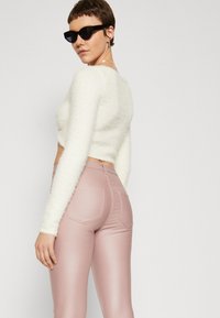 Hvit, fluffy, kort genser kombinert med tettsittende, lys rosa glinsende bukser med baklommedesign og glatt tekstur. Svart katteøye-solbriller. 