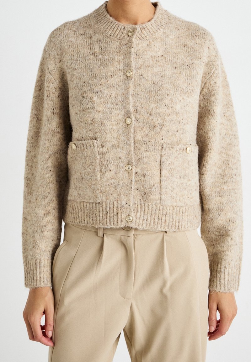 Strickjacke in hellbeige mit strukturiertem Finish, featuring einem runden Ausschnitt, Knopfverschluss und zwei Fronttaschen.
