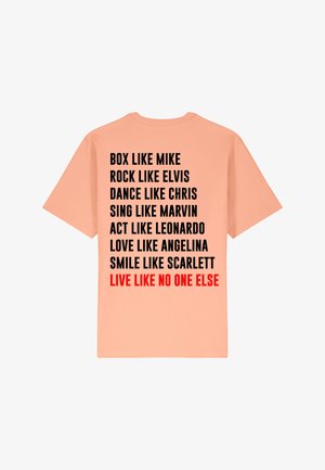 T-shirt pêche avec du texte noir et rouge au dos, illustrant des phrases inspirantes. Col rond et manches courtes. En coton.