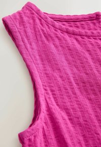 Lähivaade varrukatust erkkroosast ribiga kudumiga ülaosast, millel on kaussjooksvalgne kaelus, valgel taustal.