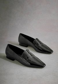 Black patent leather loafers with a pointed toe, flat heel, and a decorative strap across the upper. Smooth texture and shiny finish.