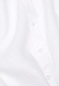 Witte linnen blouse met een zachte textuur, voorzien van kleine, doorzichtige plastic knopen en subtiele kreukels, die een soepele, lichte uitstraling laat zien.