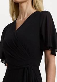 Black wrap dress with short, sheer flutter sleeves. Features a V-neckline, gathered waist with tie detail, and smooth, flowing fabric.