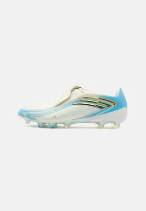 Witte voetbalschoen met blauwe en gouden accenten, flap over de veters, noppenzool voor spelen op harde ondergrond.