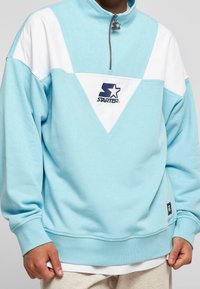 Ljusblå kvartdraget sweatshirt med vita accenter och en triangulär design. Innehåller en logotyp och ribbade muddar. Mjuk bomullsblandning.