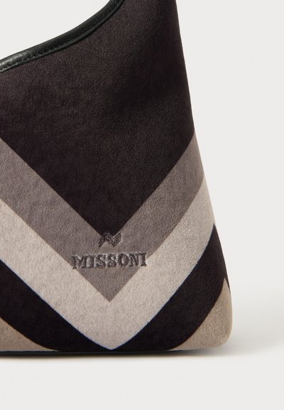 Suede torbica s chevron vzorom v temno sivi, svetlo sivi in črni barvi. Vključuje subtilno blagovno znamko in gladek, zaobljen zgornji rob.