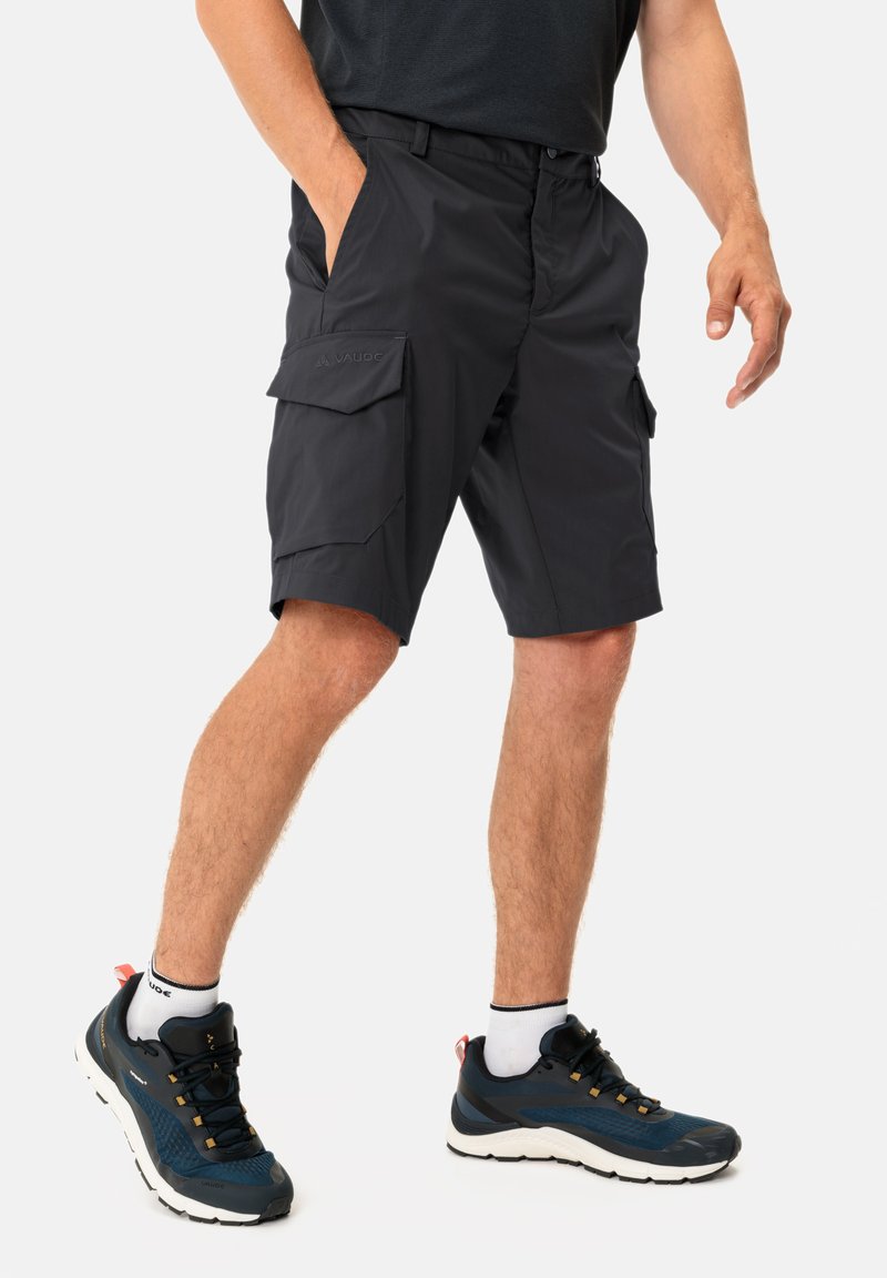 Svarta cargoshorts med en slät textur, utrustade med flera fickor, en dragkedja och en diskret logotyp framtill. Kombinerat med mörka sportskor.