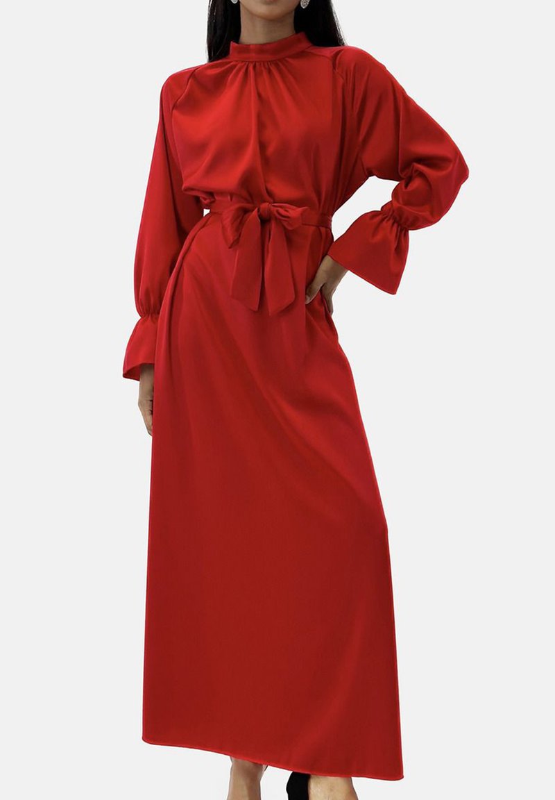 Robe rouge à manches longues avec un col montant et une ceinture nouée à la taille. Tissu doux avec une texture lisse, présentant des manches volumineuses et une coupe longue jusqu'au sol.
