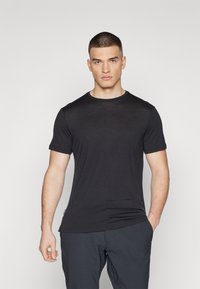 Camiseta negra de manga corta hecha de una tela suave con un escote redondo, que presenta un corte ajustado y costuras mínimas, combinada con pantalones oscuros.