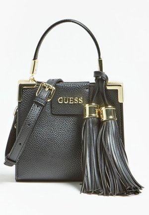 Sort tekstureret håndtaske med kort hank, gyldne hjørneaccenter, "GUESS" logo, justerbar rem og to store sorte kvaster med gyldne bånd.