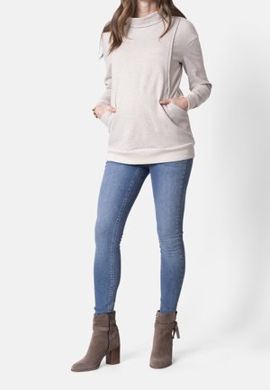 Kvinde iført beige sweater med krave og lommer, blå skinny jeans og taupe ruskind ankelstøvler med blokhæle.