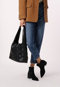 Zwarte geweven totebag met brede handvatten, gecombineerd met losse blauwe spijkerbroek en zwarte enkelboots met een gestructureerd ontwerp en blokhak.