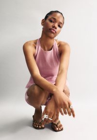 Haut à col halter de couleur rose clair avec des rayures verticales, associé à un short à motifs. Les bijoux incluent plusieurs bagues et des boucles d'oreilles créoles.