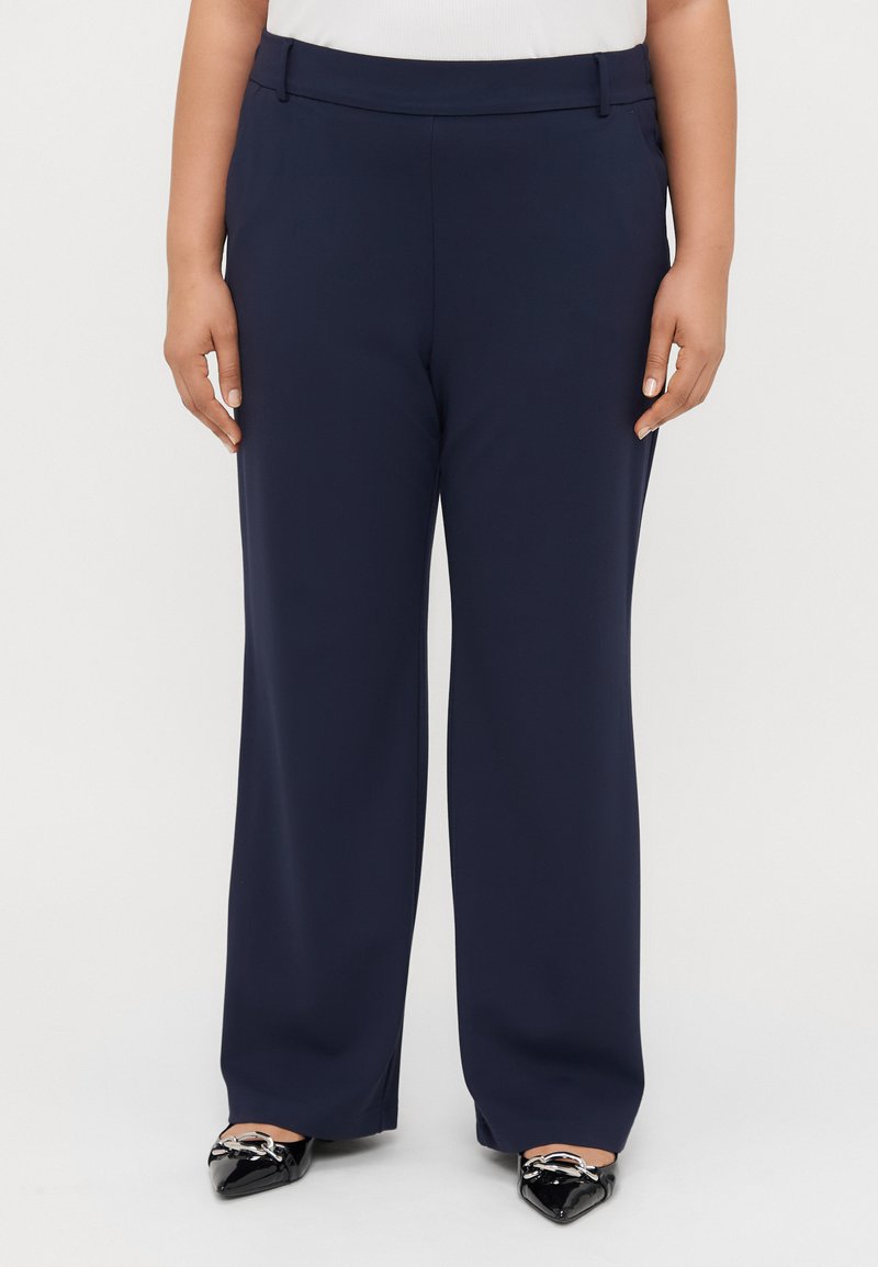 Granatowe spodnie wykonane z gładkiego materiału, o prostym kroju, z bocznymi kieszeniami i pasem, w zestawie z czarnymi szpiczastymi butami.