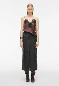 Brązowa satynowa koszulka na ramiączkach z czarnym koronkowym wykończeniem, w zestawieniu z dową, czarną skórzaną spódnicą i brązowymi botkami sięgającymi za kolano. Gładkie, błyszczące tekstury.