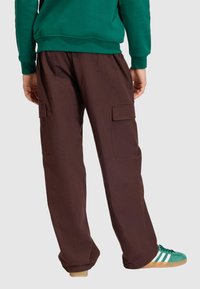 Pantalones cargo marrones con dos grandes bolsillos laterales, corte holgado y tela texturizada. Combinados con una sudadera verde y zapatillas verdes.