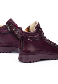 Botas de senderismo de cuero burdeos con cuello acolchado, herrajes de metal y suela de goma texturizada. Presenta un diseño de cordones y una cremallera lateral.