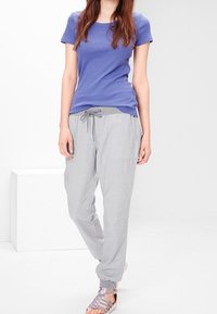 Chemise à manches courtes violette, pantalon gris clair à cordon de serrage avec poches, et sandales métalliques. Tissu léger, coupe décontractée et design relaxé.