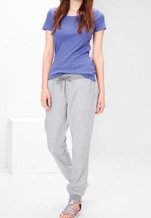 Camisa morada de manga corta, pantalones de tiro bajo en gris claro con bolsillos y sandalias metálicas. Tejido ligero, corte casual y diseño relajado.