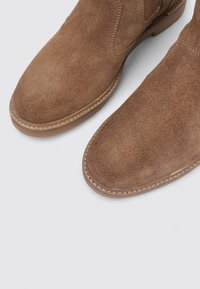 Braune Wildleder-Stiefeletten mit runder Spitze, flacher Gummisohle und genähten Details entlang des oberen Randes.