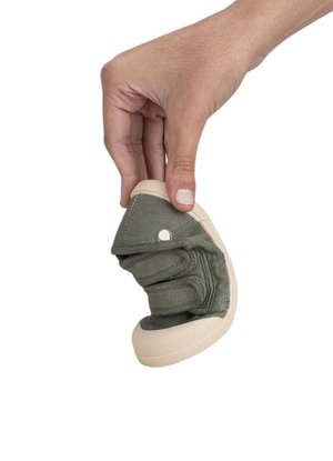 Zapato de tela verde con suela de goma crema, que cuenta con un diseño plegable, parte superior texturizada y un corte circular cerca del área de los dedos.