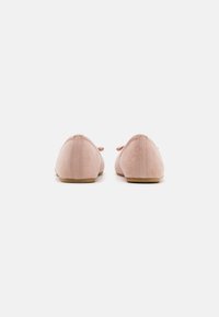 Ballerines en daim rose avec un bout rond et un petit nœud sur le devant. Semelle plate et texture lisse. Vue de dos.